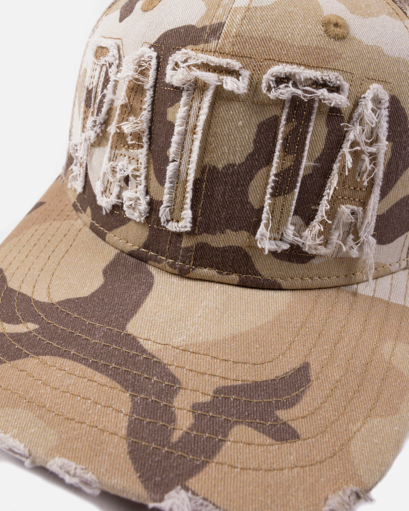 close up of the frayed branding on the woodland camo sports cap